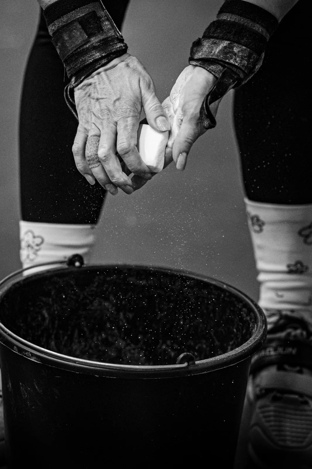EMT athlete chalking both hands above a chalk bucket before competition, black-and-white photograph