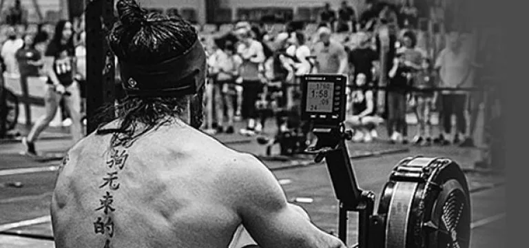 EMT competitor on a rowing ergometer during the competition, black-and-white photograph with audience in the background