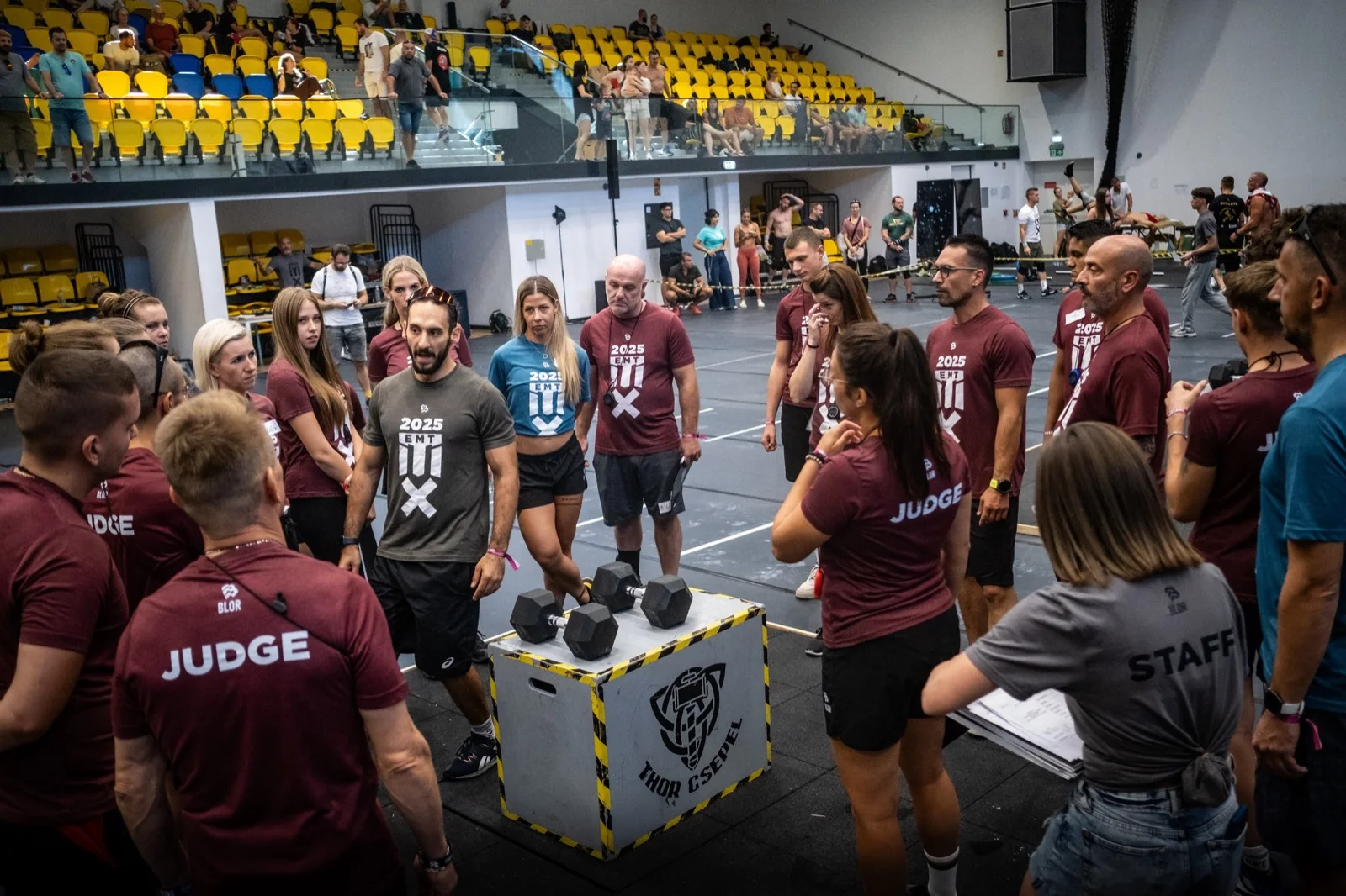 EMT 2025 finals judges and volunteer crew in a pre-event huddle in branded EMT shirts on the competition floor